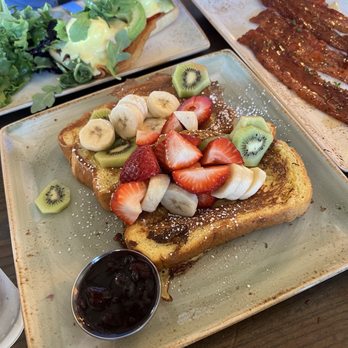 First Watch - Floridian French Toast - French toast topped with sliced bananas, strawberries, and kiwis, served with a side of blueberry syrup, on a ceramic plate. - Breakfast & Brunch Near Me - Phoenix, Arizona