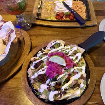 Nacho Daddy - Filet Birria Nacho and a single Cheesy Enchilada with verde in the background. Watermelon margarita too with Tajin on the rim. - Cocktail Bars Near Me - Nashville, Tennessee Nacho Daddy - Filet Birria Nacho and a single Cheesy Enchilada with verde in the background. Watermelon margarita too with Tajin on the rim. - Cocktail Bars Near Me - Nashville, Tennessee