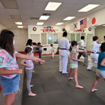 Burbank Printing - packed class! - Children and instructors are participating in a martial arts class inside a dojo, with some children practicing techniques while facing a large mirror. The room has flags from South Korea, the United States, and Japan hanging on the wall, along with martial arts weapons and decorations. The floor is covered with black mats, and the participants are wearing casual clothes or martial arts uniforms, with some children wearing face masks. - Printing Services Near Me - Burbank, California