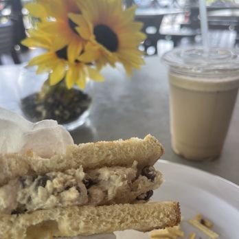 Casafinca - A sandwich with chocolate chips, a cold beverage in a plastic cup, and a sunflower in a vase are on a table at a cafe with outdoor seating. - Comfort Food Near Me - Miami, Florida