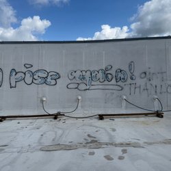 Helping Hand Roofing & Construction - A white commercial flat roof with a tall parapet wall shows spray-painted graffiti, electrical conduit running along wooden b...