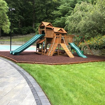 Creative Playthings - A wooden residential swing set with many slides and accessories from Creative Playthings. Shown in a rubber mulch play zone in a backyard. - Playsets Near Me - Holliston, Massachusetts Creative Playthings - A wooden residential swing set with many slides and accessories from Creative Playthings. Shown in a rubber mulch play zone in a backyard. - Playsets Near Me - Holliston, Massachusetts