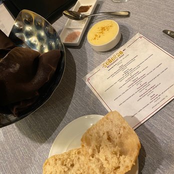 PY Steakhouse - Ciabatta bread and honey lavender butter - The image shows a table with a plate of bread, a bowl of soup, a condiment tray, and a menu at a restaurant, with a glass of water nearby. - Steakhouses Near Me - Tucson, Arizona