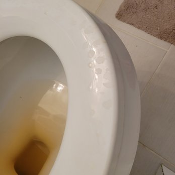 Best Yet Installations - A close-up of a toilet bowl filled with water and stains, with a beige bath mat and tiled floor visible in the background. - Electricians Near Me - Spencer, Massachusetts