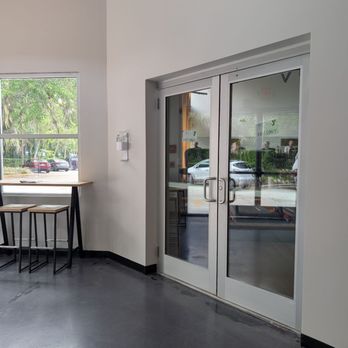 Ormond Beach YMCA - Double glass doors with metal handles open to the outside, with a window and bar-height seating area nearby inside a modern, minimalistic interior. - Gyms Near Me - Ormond Beach, Florida