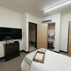 Stephanie Gardens Residential - Model room, where the bed is facing a TV on a dresser. In the corner is a door to the restroom and a closet.