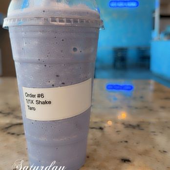 Rice Box & Boba  - Taro smoothie - A taro smoothie with a purple hue in a clear plastic cup with a dome lid and straw, placed on a marble countertop. - Laotian Near Me - Albuquerque, New Mexico
