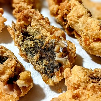 Mel & Libby's Catering - fried food - Close-up image of fried fish fillets with a golden, crispy breading. One fillet is partially broken, revealing the flaky white fish inside and dark skin. The fillets are arranged on a white surface, highlighting the texture of the fried coating. - Caterers Near Me