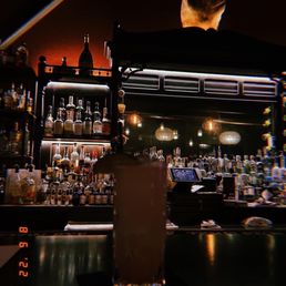 Bar - A tall cocktail glass with a drink and straw is placed on a bar counter, with a background of liquor bottles and warm ambient lighting.