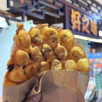 Yummie - Yummie - egg waffles - A bubble waffle is held in a paper bag in front of a storefront with Chinese characters, likely in Toronto. - Candy Stores Near Me - Toronto, Ontario