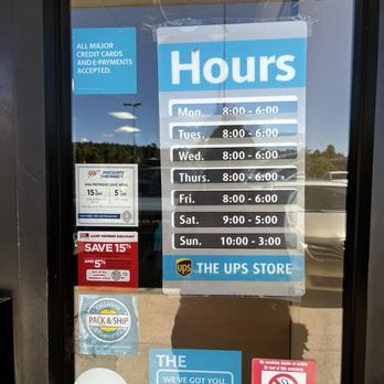The UPS Store - Posted store hours - A glass door displays store hours for The UPS Store in Flagstaff, AZ, along with various promotional stickers and notices. - Shipping Centers Near Me - Flagstaff, Arizona
