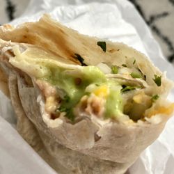Bean and cheese burrito with cilantro and onions added, topped with avocado sauce