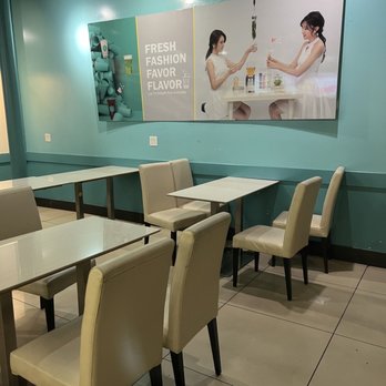 T4 - 11/16/22 Interior - A dining space with beige upholstered chairs and white tables, featuring a large promotional poster on a teal wall. - Tea Rooms Near Me - San Leandro, California
