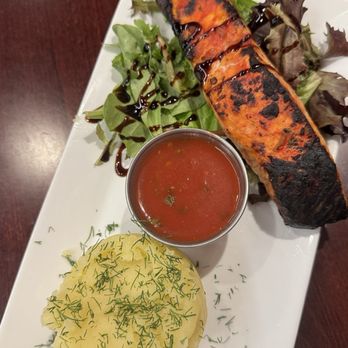 Georgian Chef - Salmon - A plate features a grilled salmon fillet with grill marks, a side salad with balsamic drizzle, a small cup of tomato-based soup, and mashed potatoes garnished with herbs. - Georgian Near Me - Howell, New Jersey
