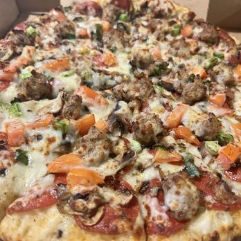 Pizza Leon - Large garlic Combination 14" - A close-up of a pizza with toppings including sausage crumbles, diced tomatoes, chopped green onions, and melted cheese. The pizza is in a cardboard box, showing a variety of fresh ingredients and a baked crust. - Pizza Near Me - Austin, Texas