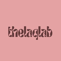The image features a logo with the word 'thelaqlab' written in a unique, stylized font in dark brown color. The background is a solid light pink, creating a contrast that highlights the text. The design is simple and centered, with no additional elements or imagery.