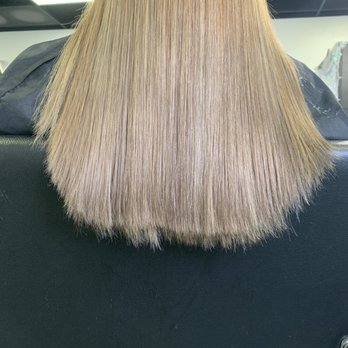 Alison The Barber - This is what a $45 haircut will get you. - The image shows the back of a person with straight, blonde hair that reaches just past the shoulders. The hair appears smooth and well-maintained, with a shiny finish. The setting is a salon, indicated by the black salon chair and the professional lighting overhead. The background includes salon elements such as ceiling panels and possibly other salon equipment, but they are out of focus. - Barbers Near Me - Albuquerque, New Mexico