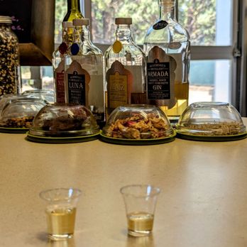 Algodones Distillery - Alcohol bottles and small tasting cups are displayed on a counter at Algodones Distillery, with a window showing trees outside. - Distilleries Near Me - Algodones, New Mexico