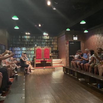 Drunk Shakespeare - Chicago - The stage - People sit on benches in a theater setting with a large bookshelf backdrop and a throne at the front, likely for a performance or event. - Performing Arts Near Me - Chicago, Illinois