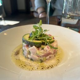 Hamachi Ceviche - A dish of hamachi ceviche with diced fish, topped with avocado slices and microgreens, served on a white plate.