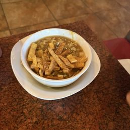 Hot Sour Soup - A bowl of sweet and sour soup with vegetables and fried wonton strips, served on a white plate at a restaurant.