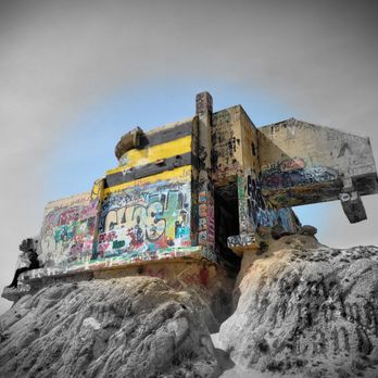 Devil's Slide Historical Landmark/viewpoint - The image features a concrete structure covered in colorful graffiti, positioned on a rugged, rocky terrain at Devil's Slide. The structure appears weathered and is set against a partly cloudy sky, with a faint blue hue visible behind the structure. The scene emphasizes the contrast between the urban graffiti art and the natural rocky environment. - Landmarks & Historical Buildings Near Me - Pacifica, California