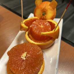 A white plate holds slices of orange and carved fruit decorations, including a bear-shaped orange and a flower-shaped fruit, on a wooden table.