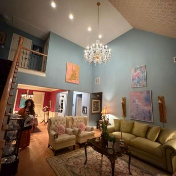 TRU Lighting & Electrical Services - A vaulted living room with blue walls showcases a large crystal chandelier, recessed lighting, abstract artwork, tufted wingb... - Electricians Near Me - Holly Springs, Georgia TRU Lighting & Electrical Services - A vaulted living room with blue walls showcases a large crystal chandelier, recessed lighting, abstract artwork, tufted wingb... - Electricians Near Me - Holly Springs, Georgia