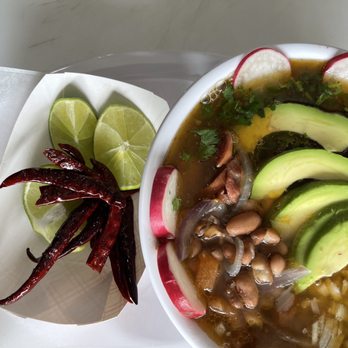 El Pollo Cris Cris - A bowl of Mexican-style soup topped with avocado slices, radish, cilantro, and beans, served with lime wedges and dried chili peppers on the side. - Mexican Near Me - Chicago, Illinois