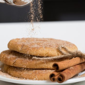 Tiffs Treats - a person sprinkling cinnamon powder on a stack of cookies - Desserts Near Me - Fort Worth, Texas