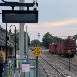 LIRR Station - Train Schedule Display (scrolled in picture). Background: train cars from Railroad Museum of Long Island