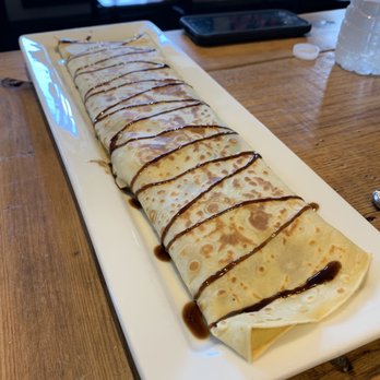 Cafe e Dolci - Balsamic chicken - A long, rolled crepe dessert topped with chocolate sauce is served on a rectangular white plate, placed on a wooden table. - Themed Cafes Near Me - Franklin, New Jersey