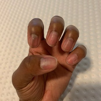 Happy Nails - The image depicts a close-up of a hand with dark skin tone, showing natural, unpainted nails. The hand is positioned with fingers slightly curled, resting on a textured white surface that appears to be fabric or a mat with small raised dots. The lighting is even, highlighting the skin's texture and the nails' natural appearance. - Nail Salons Near Me - Slidell, Louisiana