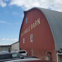 A large red barn with the sign 'Old Candle Barn' on its side, featuring small windows and a curved roof, with parked cars in front.