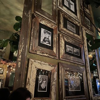 Samba Montclair - A wall features several weathered wooden picture frames with black-and-white photographs, set in a rustic interior with plants and decorative lighting. - Brazilian Near Me - Montclair, New Jersey