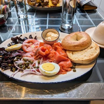 CDA - This looked fantastic - my sister savoured every luxurious bite. - A breakfast plate featuring smoked salmon, a halved boiled egg, a bagel, a small dish of butter, and a salad with lettuce, tomato, onion, and capers, on a ceramic platter. - French Near Me - Chicago, Illinois