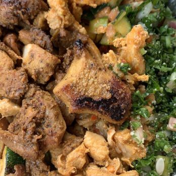 Marhaba - The image shows a foil takeout container filled with fried meats, including pieces of chicken and possibly lamb, alongside chopped vegetables and herbs such as parsley and green onions. The food appears freshly cooked, with crispy textures on the fried items and vibrant green herbs adding freshness. The container suggests a meal typical of Middle Eastern or Mediterranean cuisine, served for takeout or delivery. - Mediterranean Near Me - McLean, Virginia