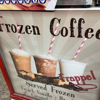 Maple Shade Custard Stand - The sign features three images of frozen coffee drinks in clear cups with red and white striped straws. The drinks are labeled as served frozen with flavors including French Vanilla, Hazelnut, Caramel, and Mocha. The background has a light, striped pattern, and the sign emphasizes the word 'Frappe!' in red. The lower part of the sign shows a decorative chocolate and caramel drizzle with small pieces of caramel or toffee. - Ice Cream & Frozen Yogurt Near Me - Maple Shade, New Jersey