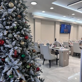 Grace Nails - A Christmas tree with ornaments is positioned in a modern nail salon with white chairs and tables, and a TV screen on the wall. - Nail Salons Near Me - Silver Spring, Maryland