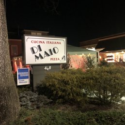 Nighttime photo of a restaurant sign for Di Maio Italian Cuisine and Pizza, with bushes and a tree in the foreground.