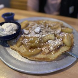 Old Dutch - A plate featuring a Dutch pancake with apple slices, dusted with powdered sugar, accompanied by a small bowl of ice cream, on a wooden table.