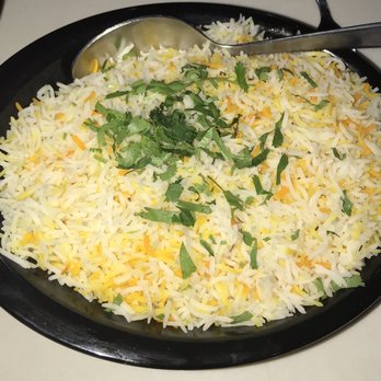 Shaahi Biryani - Plain Rice - A black oval plate contains cooked rice with shredded cheese and chopped cilantro on top, served with a metal spoon. - Indian Near Me - Glendale Heights, Illinois