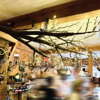 Candlestock - Glow Flow - A branch decorated with string lights is suspended from the ceiling in a candle shop, with blurred figures below and shelves of candles and decor. - Home Decor Near Me - Woodstock, New York