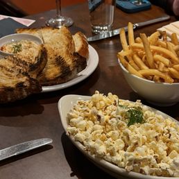 Smoked Trout - The image shows a restaurant table with toasted bread slices, a bowl of French fries, and a dish of popcorn, with drinks and utensils in the background.