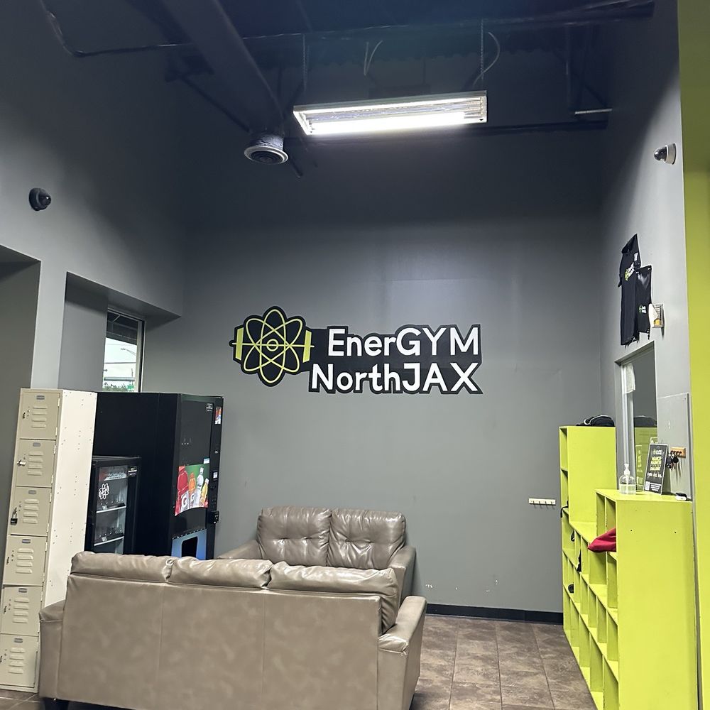 EnerGYM NorthJAX - Waiting/lounge area at EnerGYM NorthJAX with couches, vending machines, lockers, and the gym logo on the wall. - Gyms Near Me - Jacksonville, Florida EnerGYM NorthJAX - Waiting/lounge area at EnerGYM NorthJAX with couches, vending machines, lockers, and the gym logo on the wall. - Gyms Near Me - Jacksonville, Florida