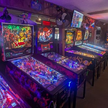 Fast Eddie's MOAB - Pinball for dayz! - Multiple pinball machines and arcade game cabinets are arranged in a row inside a retro-themed gaming arcade, with colorful lighting and vintage decor. - Fast Food Near Me - Modesto, California