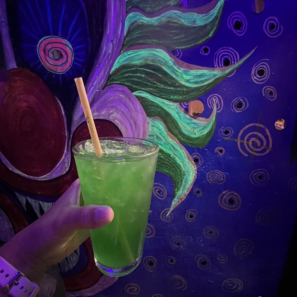 Wonderland - a hand holding a green drink with a straw - Dive Bars Near Me - Richmond, Virginia