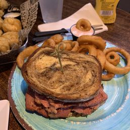 Pastrami sandwich with onion rings. Fried mushrooms in the back. Pastrami sandwich with onion rings. Fried mushrooms in the back.
