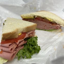 Avril-Bleh & Sons Meat Market - Freshly crafted sandwich, with white bread, fresh lettuce and tomato, pickles and mustard, and a large portion of sliced olive loaf meat.