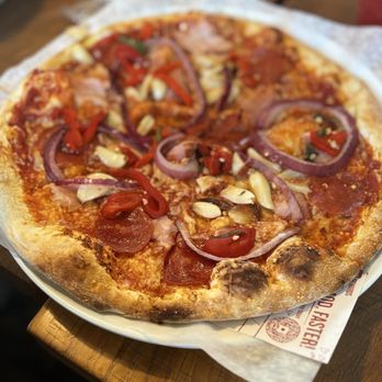 MOD Pizza - A pizza with pepperoni, red onions, garlic, and red peppers, served on a plate with parchment paper, placed on a wooden table. - Pizza Near Me - Tucson, Arizona